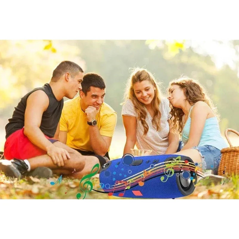A blue, cylindrical portable waterproof Bluetooth speaker in the foreground, with friends enjoying music in a park.