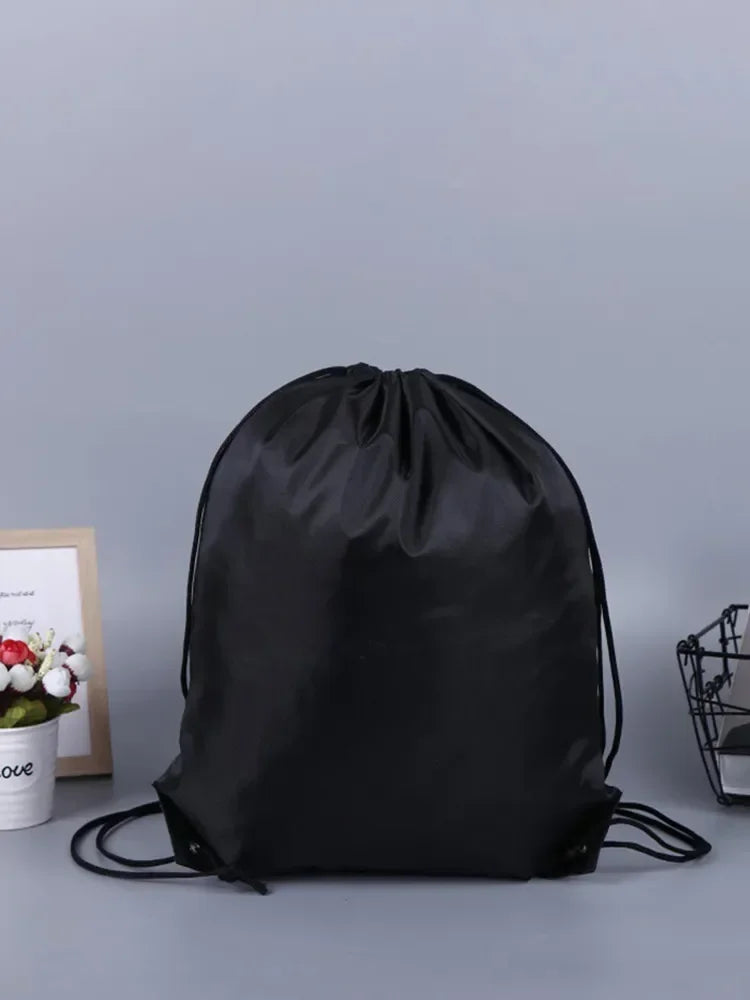 Plain black drawstring bag with adjustable rope straps, set against a grey background.