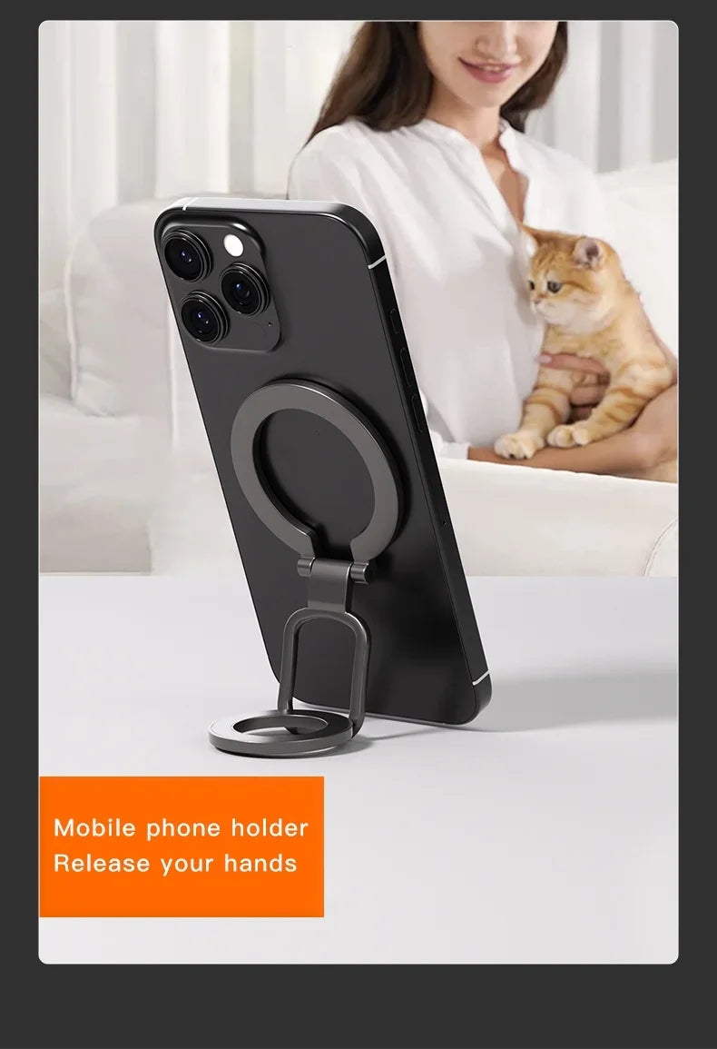 A matte black, foldable ring-style mobile phone holder attached to the back of a black smartphone on a white surface.