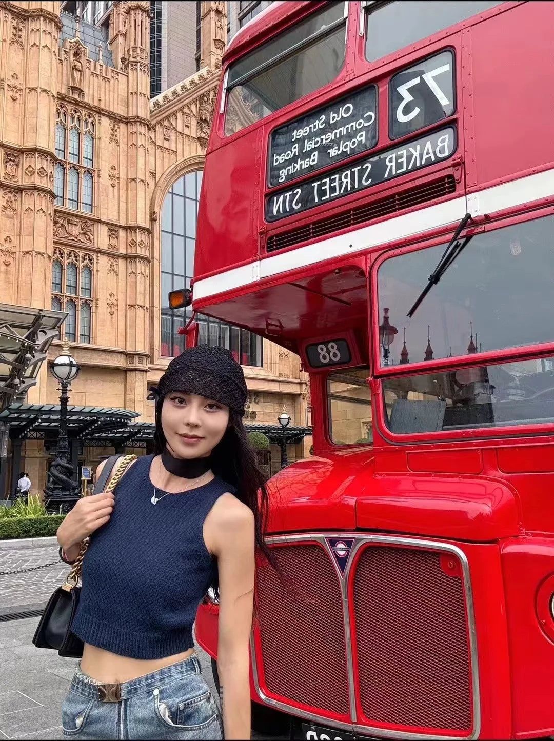 A woman wearing an elegant black knitted hat with a side bow, standing in front of a red London bus.