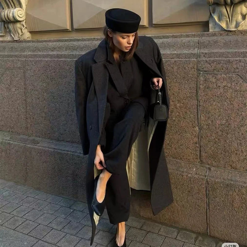 Elegant black wool pillbox-style hat worn by a model in a smart, tailored charcoal coat and trousers.