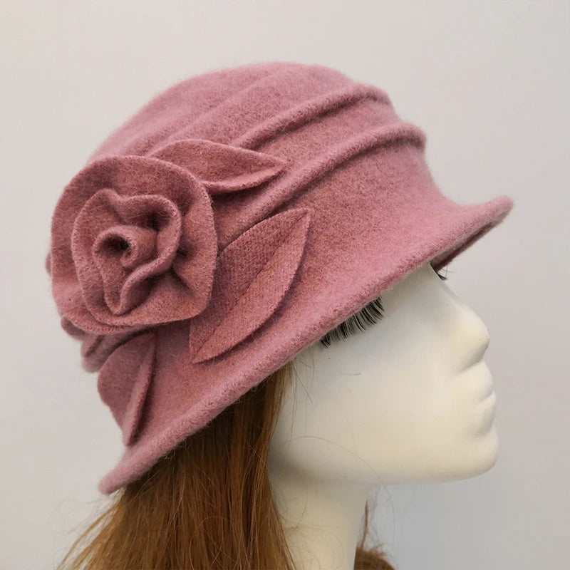Elegant dusty pink wool cloche-style winter hat featuring a decorative fabric rose and leaf detail on a mannequin.