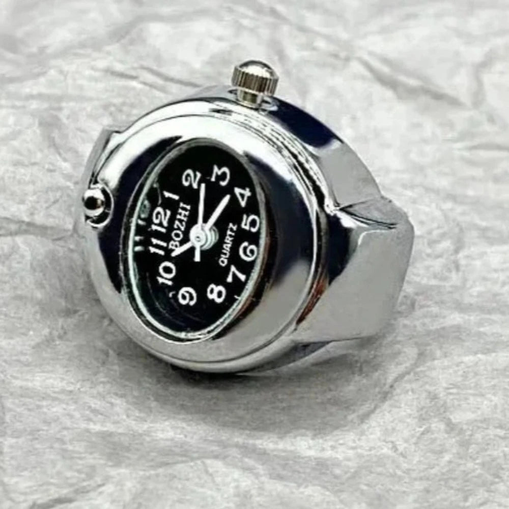 A polished silver-tone analogue watch ring with a round black face and white numeral markers.