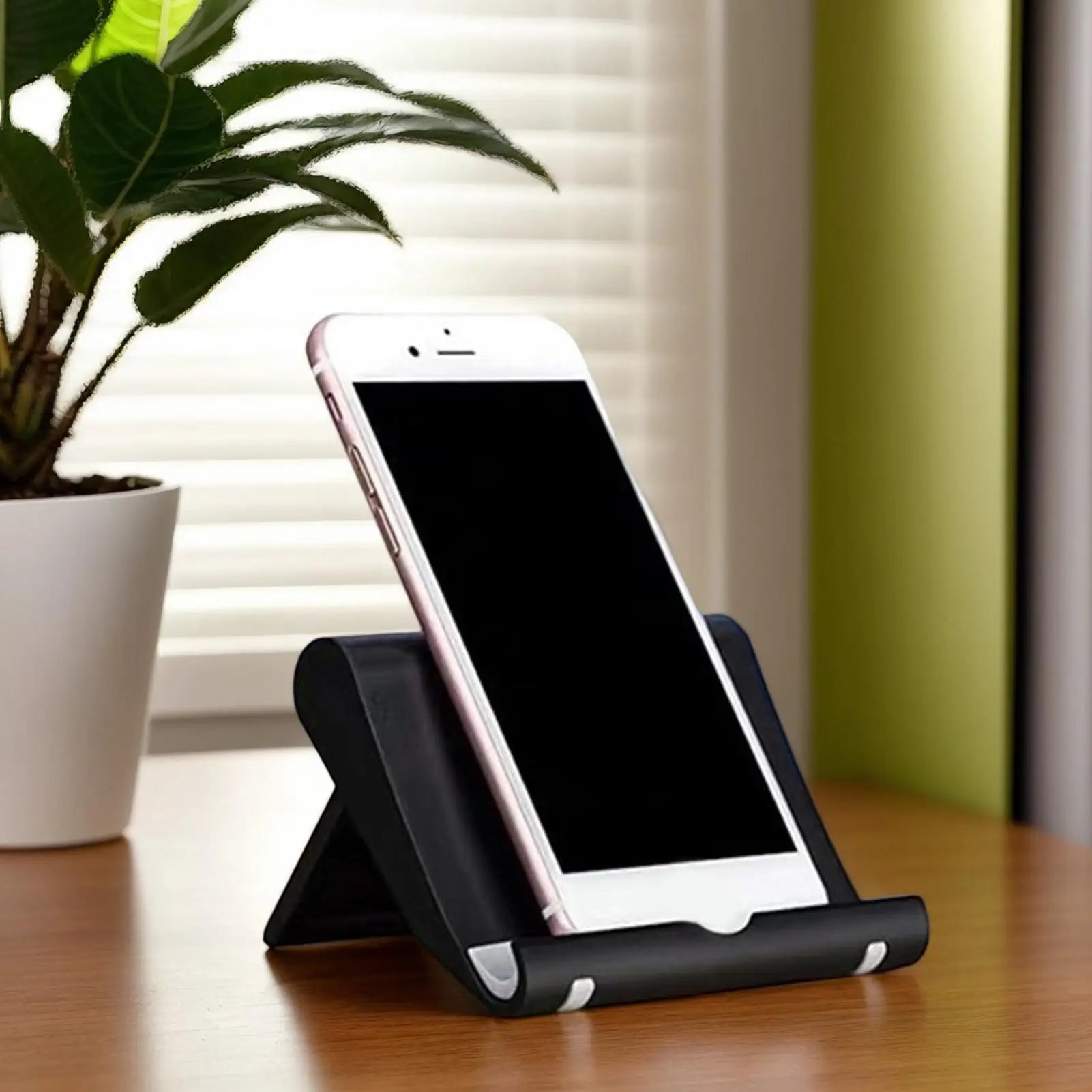 Black adjustable desktop mobile phone stand holding a smartphone upright on a wooden desk.