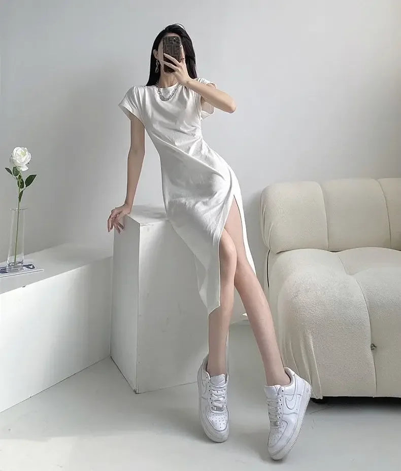 Woman wearing a white, short-sleeved midi dress with a high side slit, paired with white trainers.