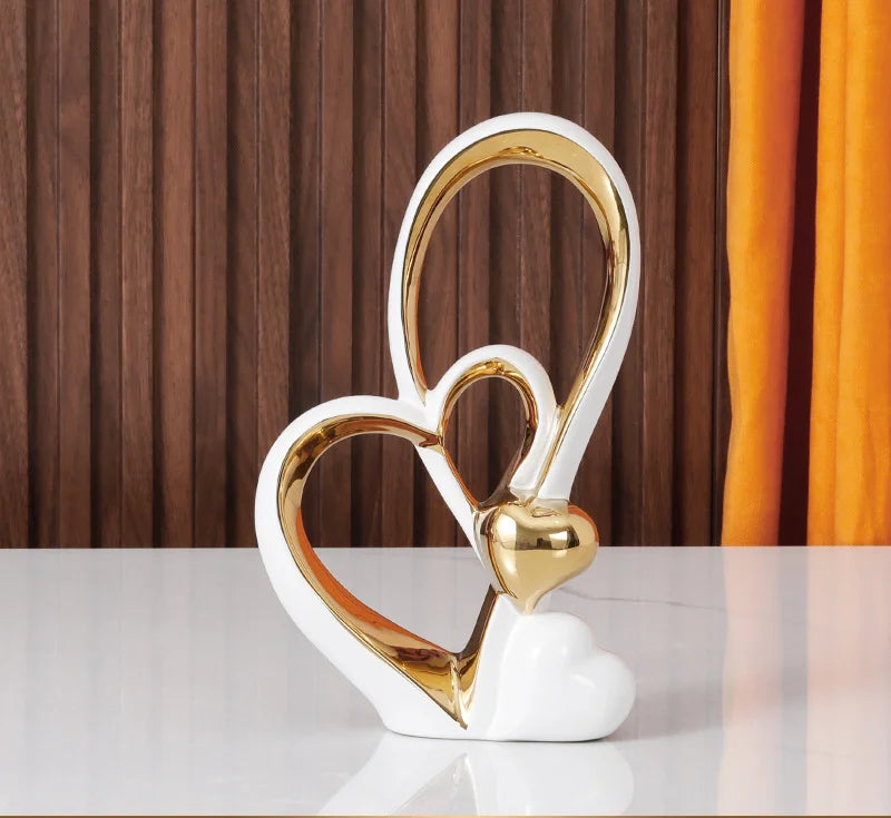Modern ceramic ornament featuring white and gold interlocking heart shapes on a white table.