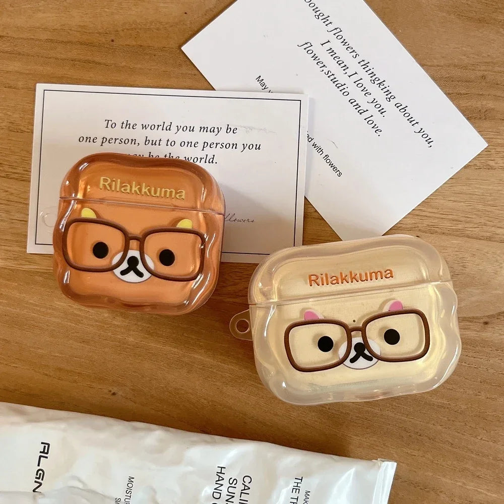 Two clear plastic Rilakkuma character AirPod cases in brown and cream, featuring glasses design.