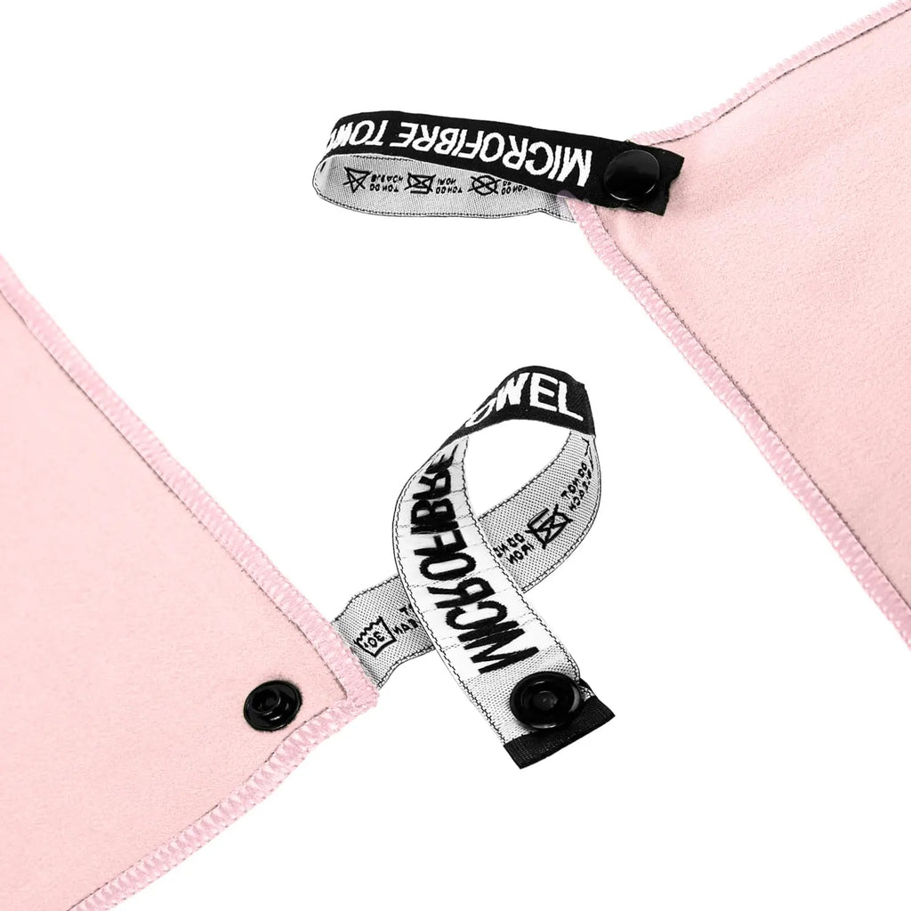 Close-up of a pale pink microfibre towel with black popper fasteners and branded fabric hanging loops.