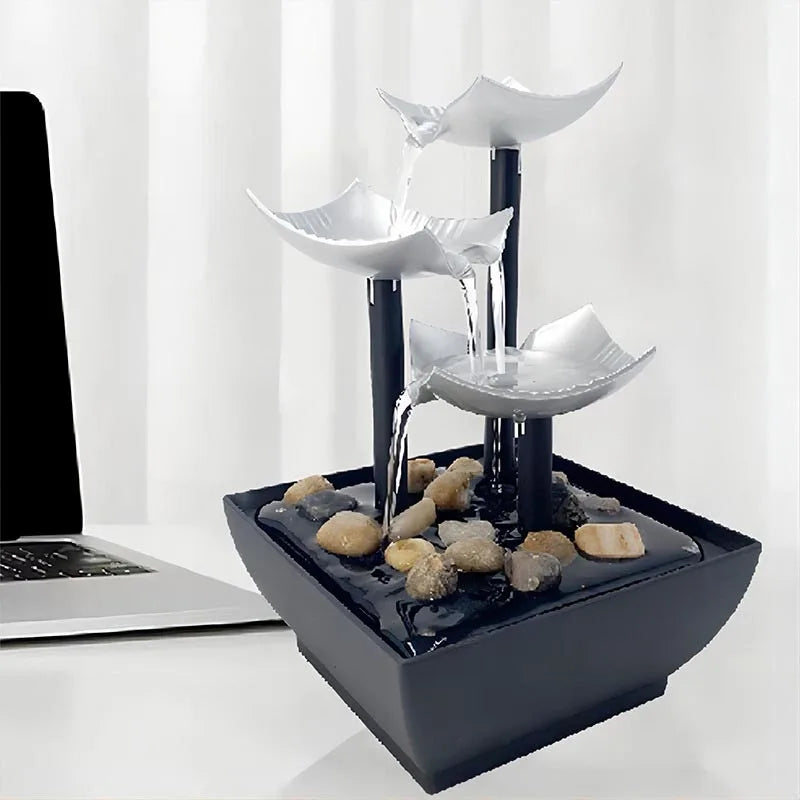 Modern indoor tabletop fountain with three silver leaf-shaped tiers, black stands, and decorative river stones.