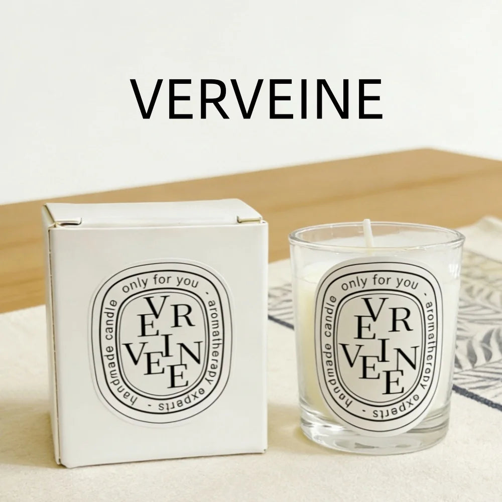 A white Verveine-scented aromatherapy candle in a glass jar, next to its matching white square presentation box.