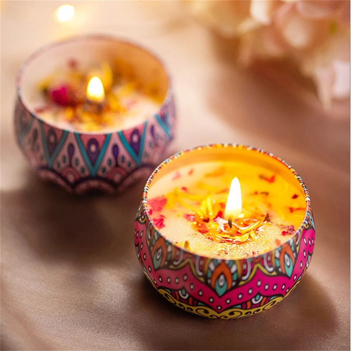 Two lit, scented candles in colourful patterned metal tins decorated with dried flower petals.