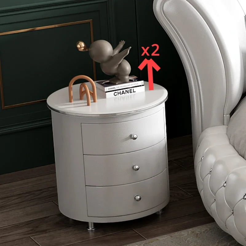 Modern, circular white bedside table with three drawers, silver handles, and a sleek, luxurious finish.