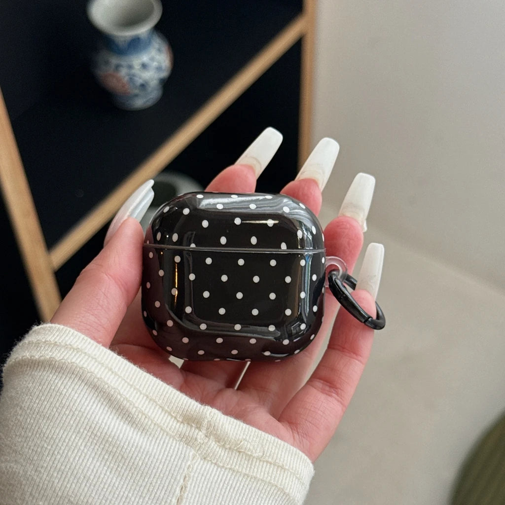 Black and white polka dot glossy AirPods case with matching keyring, held in hand.