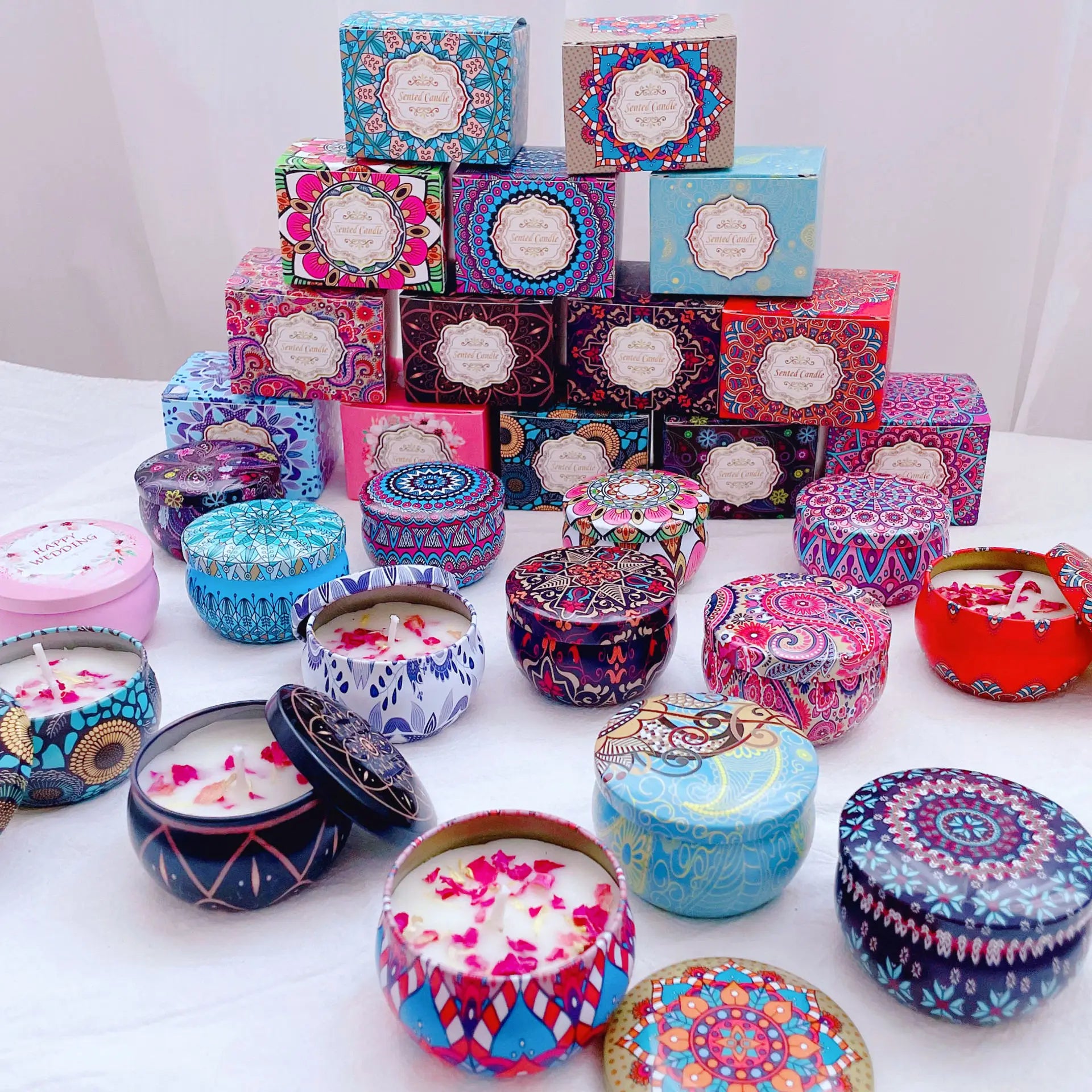 Assorted colorful scented candles in decorative metal tins with matching patterned gift boxes on a white background.