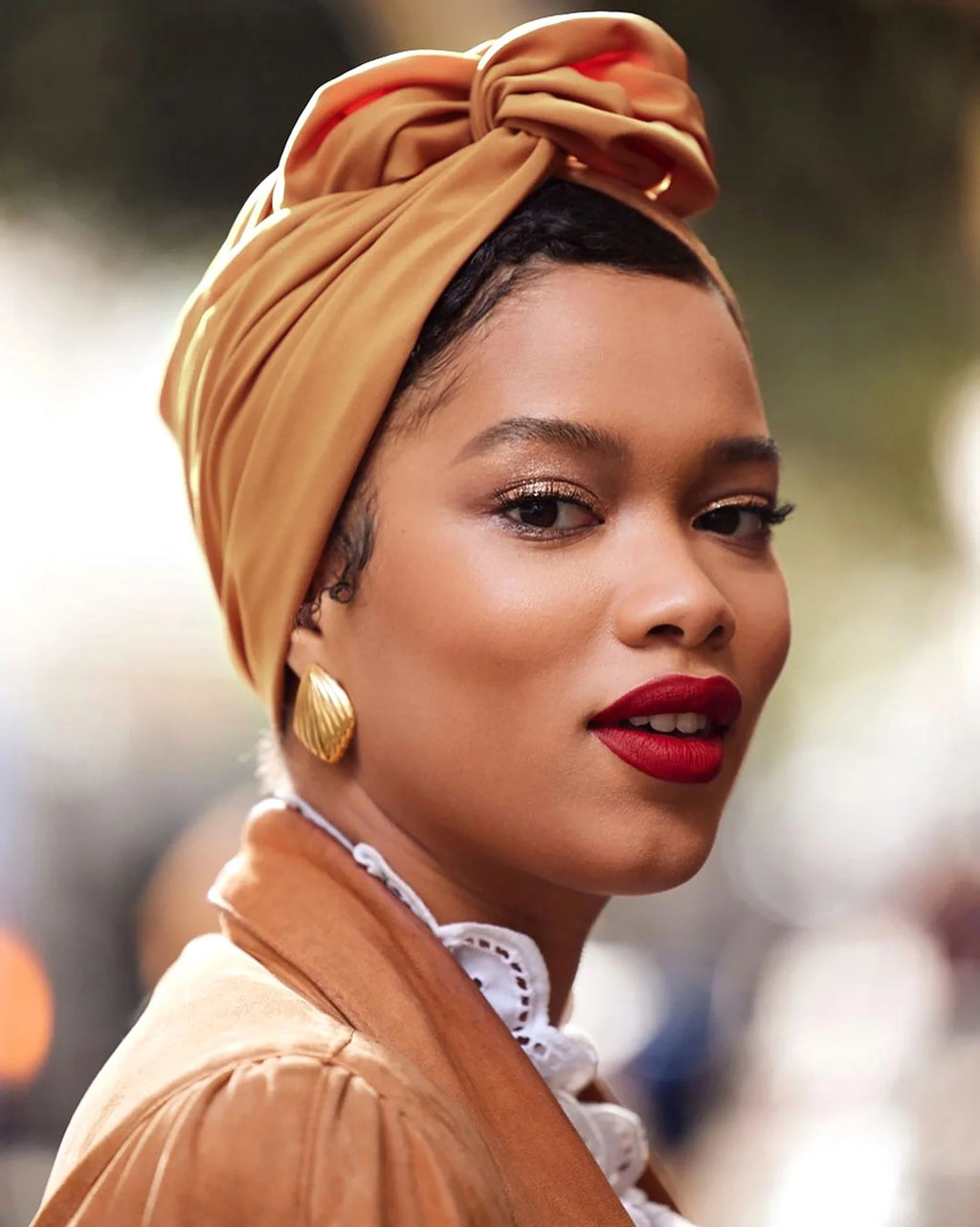 A model wearing a vintage-style, mustard-yellow knotted turban hat with elegant draped detailing.