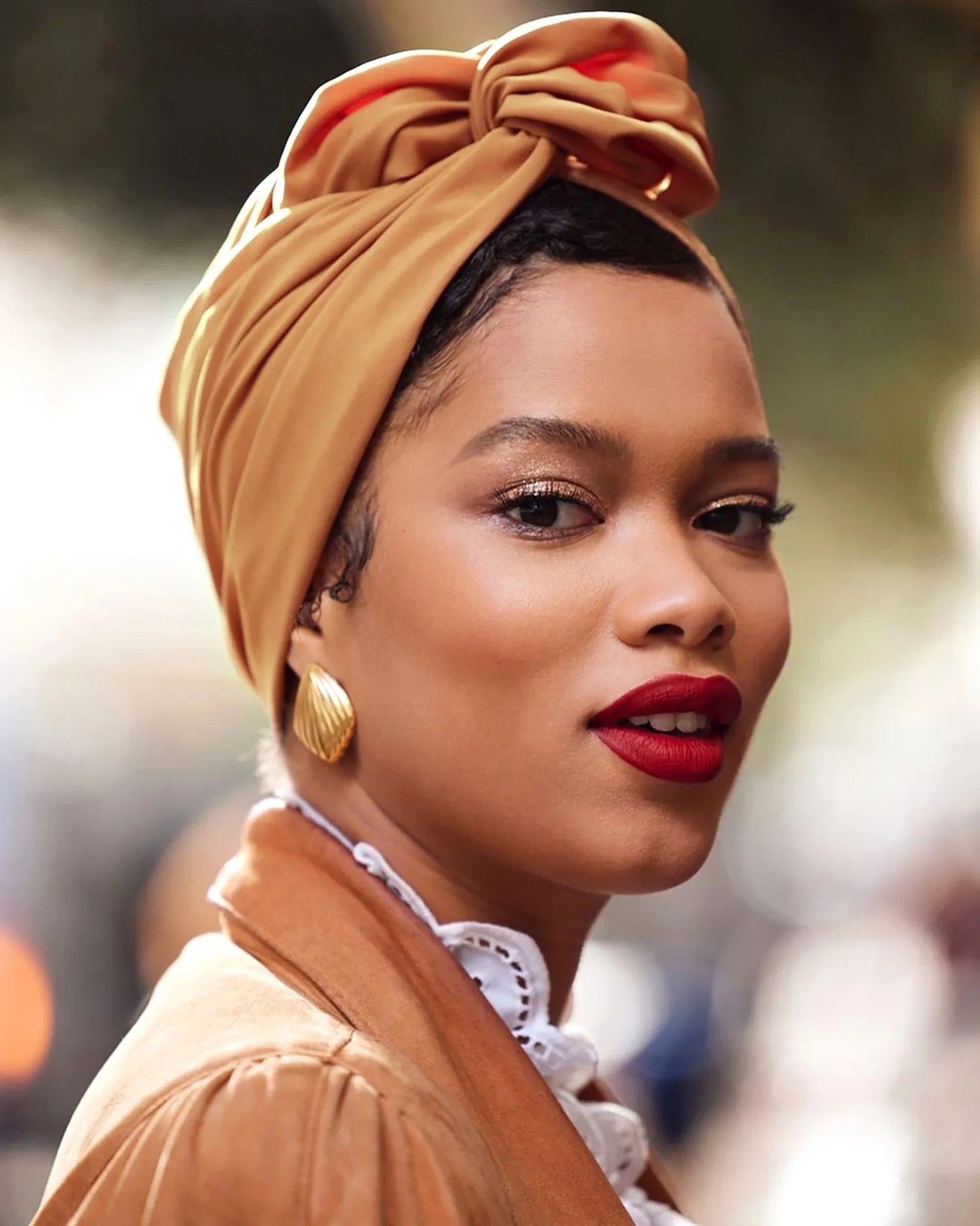 A model wearing a vintage-style, mustard-yellow knotted turban hat with elegant draped detailing.