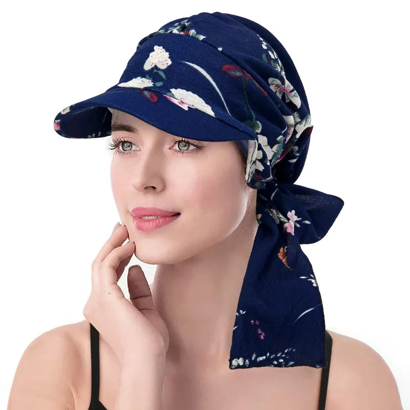 A woman wears a navy blue floral print headscarf hat with a sun brim and a tie detail at the back.