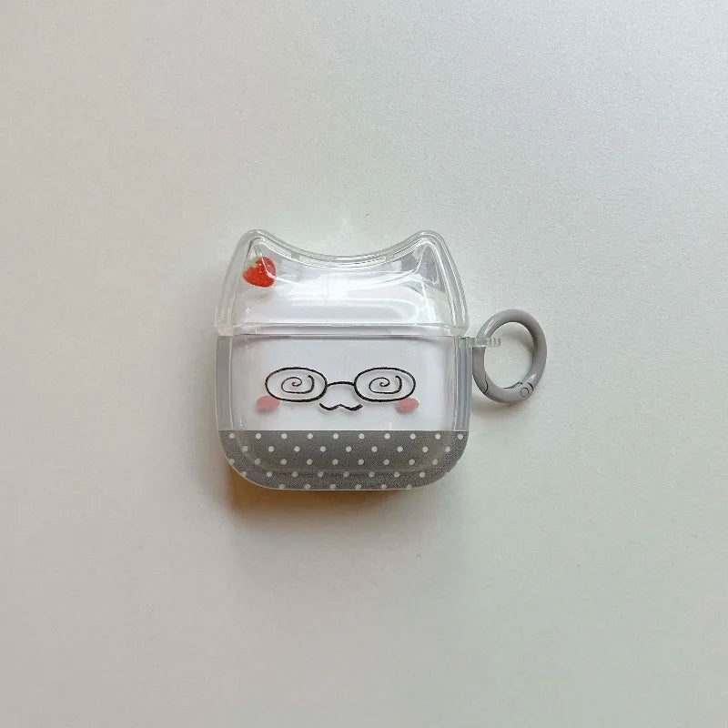 Clear silicone AirPods case with cat ears, glasses face, polka dot pattern, strawberry charm, and grey keyring hook.