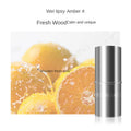 Silver cylindrical roller ball perfume bottle with brand text, set against a background of fresh sliced oranges.