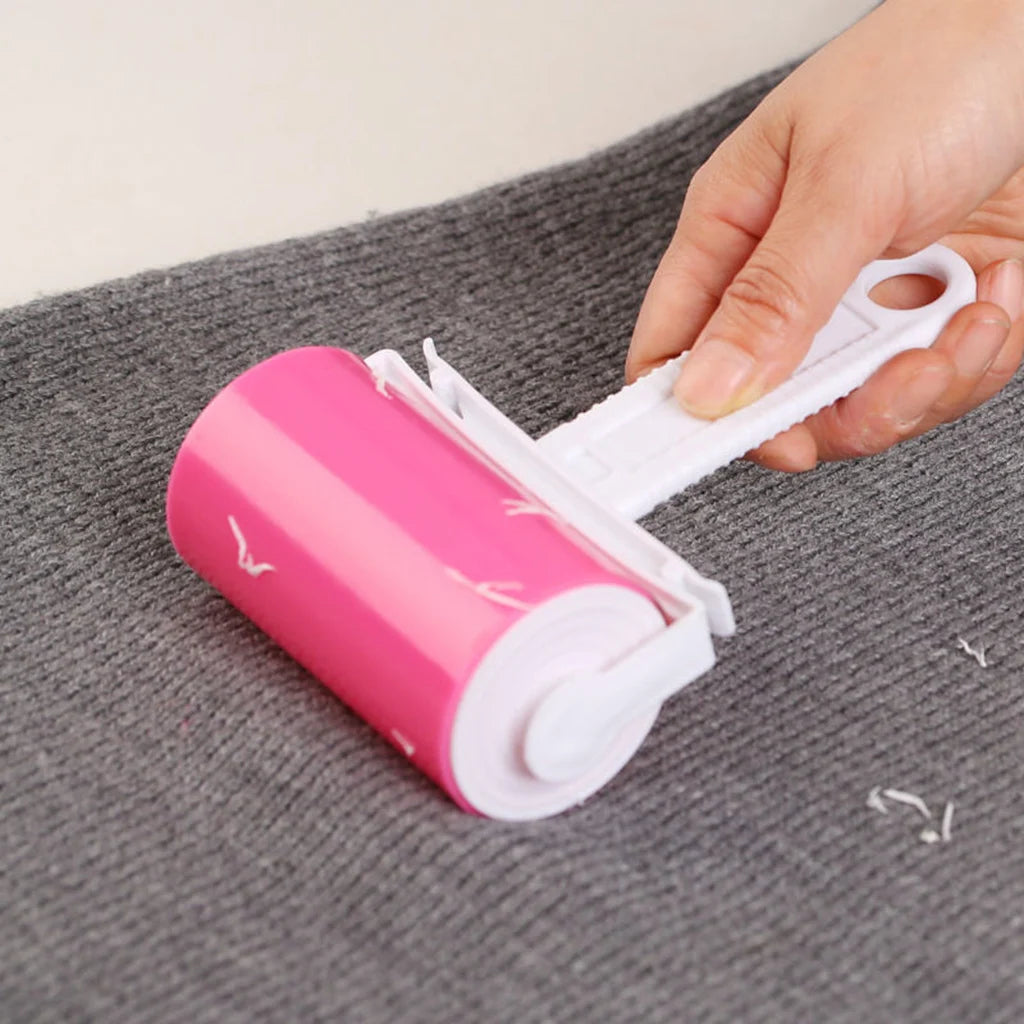 Hand using a pink adhesive lint roller to remove fuzz from a grey knitted fabric.