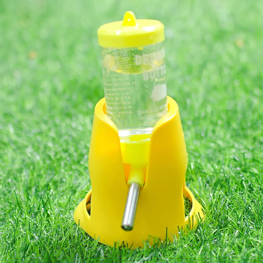 Yellow pet water dispenser with a clear bottle and stainless steel nozzle, standing on a green grass background.