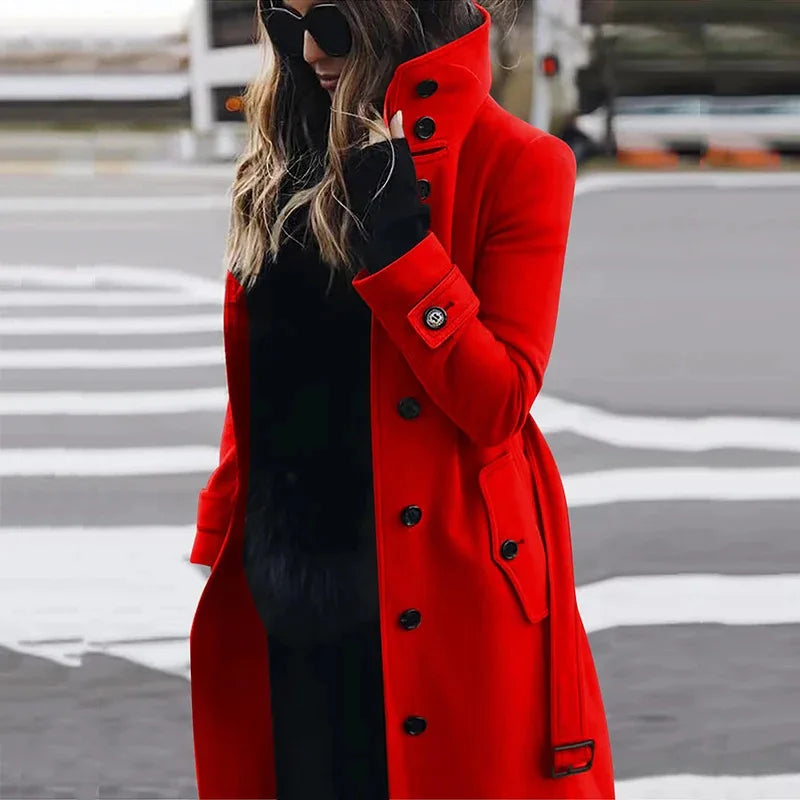 A woman wears a vibrant red, knee-length tailored coat with a high collar, black button details, and cuffs.