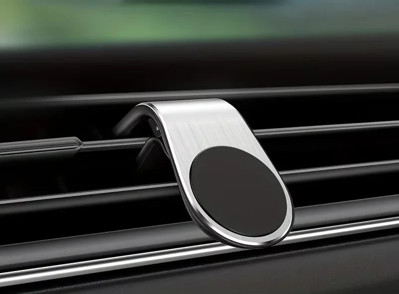 A brushed silver magnetic car phone mount attached to a vehicle air vent, featuring a circular black surface.