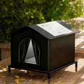 Black outdoor cat house on a raised stand with a waterproof pitched roof and arched curtained entrance.