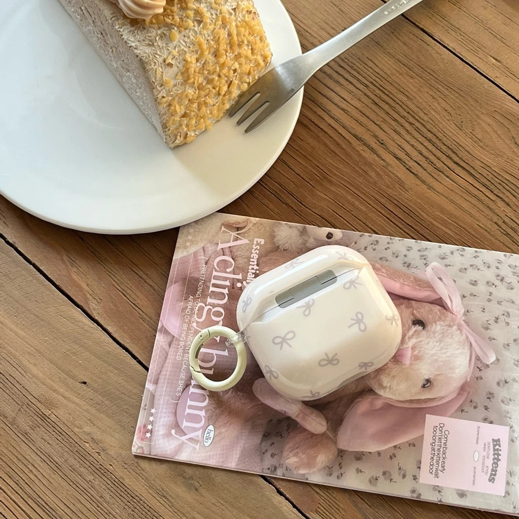 White AirPods Pro case featuring a dainty grey bow print, smooth finish, and a matching clip attachment.
