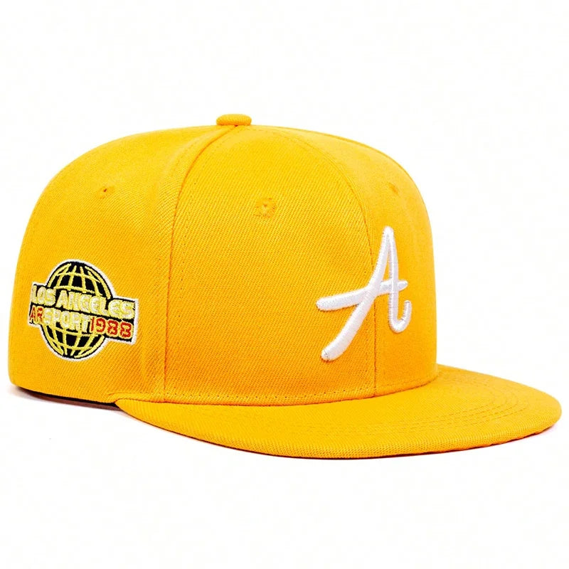 Bright yellow baseball cap with a white embroidered letter 'A' and a globe graphic detail on the side.