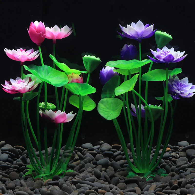 Artificial pink and purple lotus flowers with green leaves and stems planted in a bed of dark aquarium pebbles.