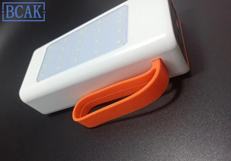 White portable power bank with integrated LED light panel and an orange silicone carry strap.