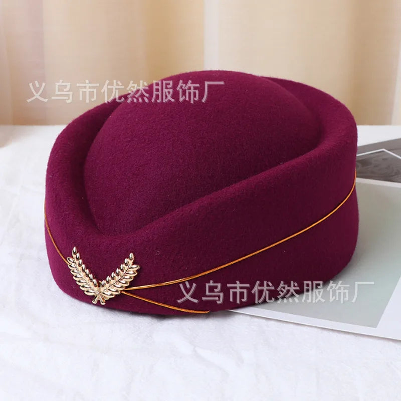 Deep burgundy felt pillbox stewardess hat with a gold trim detail and decorative metallic leaf emblem.