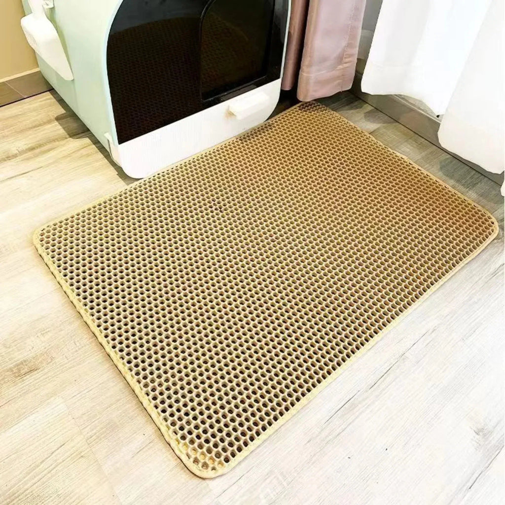 Tan, heavy-duty waterproof cat litter mat with a honeycomb mesh design, placed on a wooden floor by a litter box.