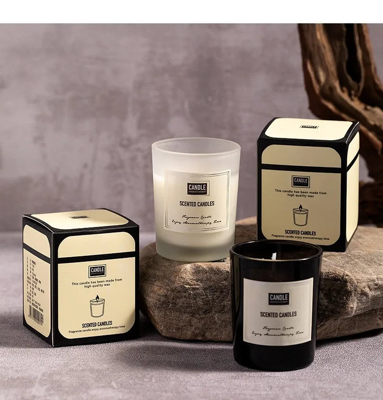 Two scented candles in matte black and frosted white glass jars, each displayed next to its matching cream-colored box.