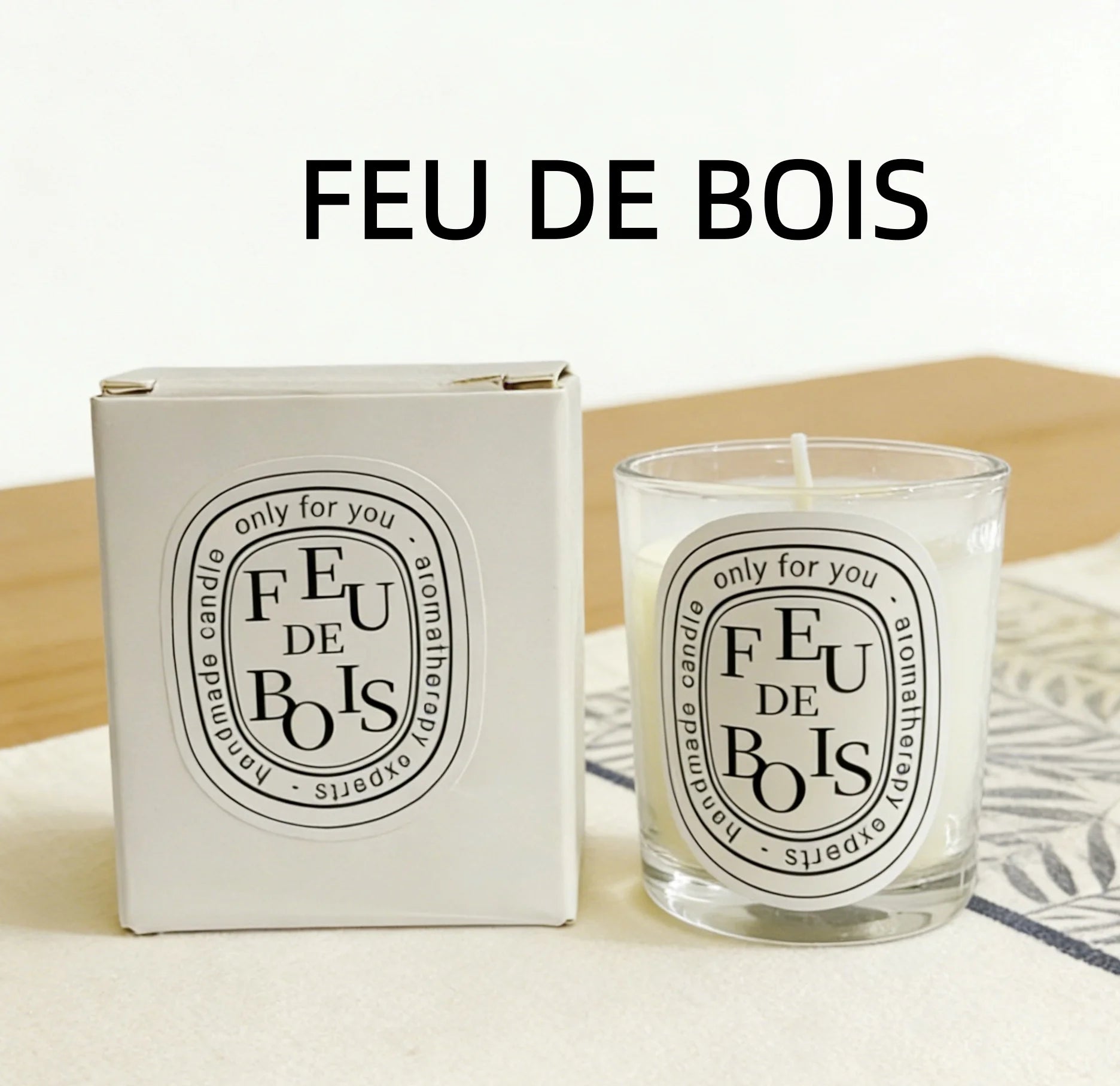 Feu de Bois scented candle in a glass votive with matching white gift box, featuring minimalist black oval labels.