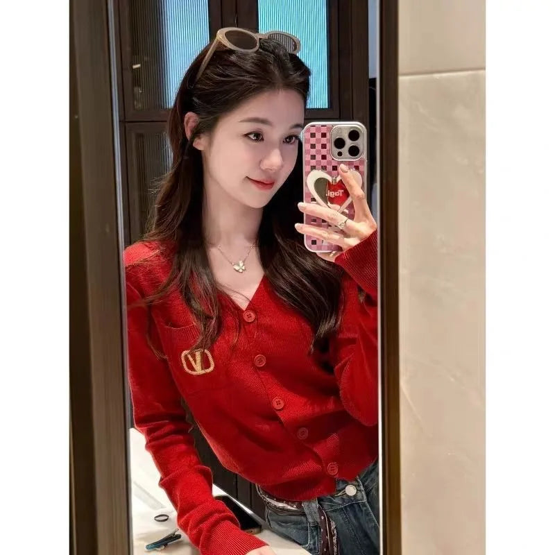Woman wearing a vibrant red, V-neck knitted cardigan with gold-tone button fastening and a chest pocket detail.