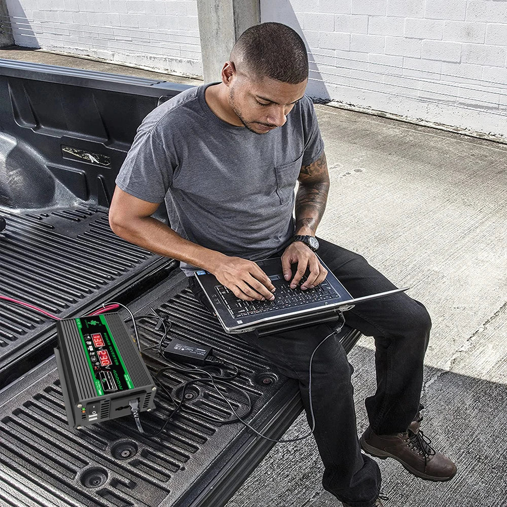 Man working on a laptop in a truck bed, powered by a black 400W portable power inverter with a digital display.