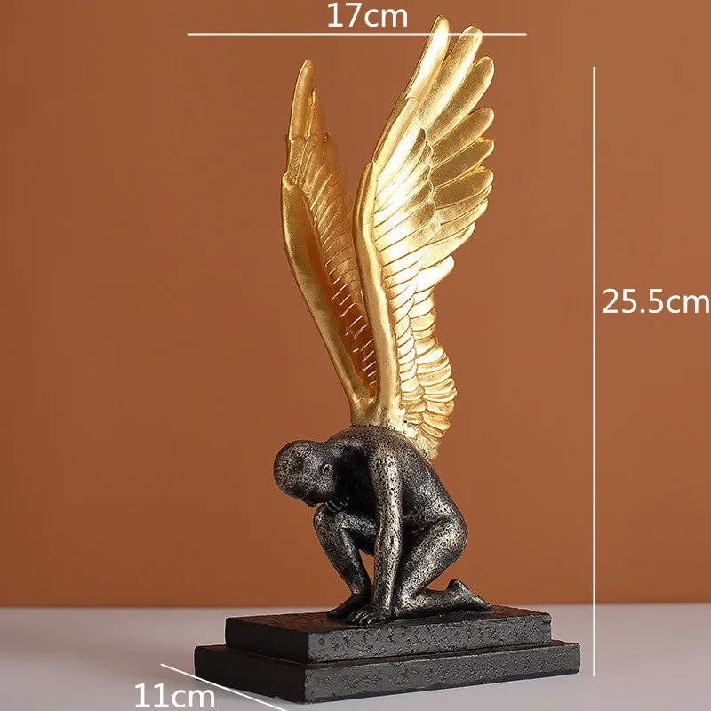 Decorative ornament featuring a kneeling dark textured figure with large, detailed gold wings on a black rectangular base.