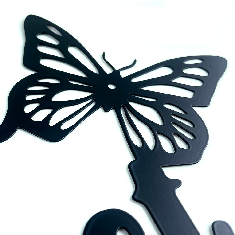 Close-up of a matte black metal wall art piece featuring a decorative cutout butterfly design on a white background.