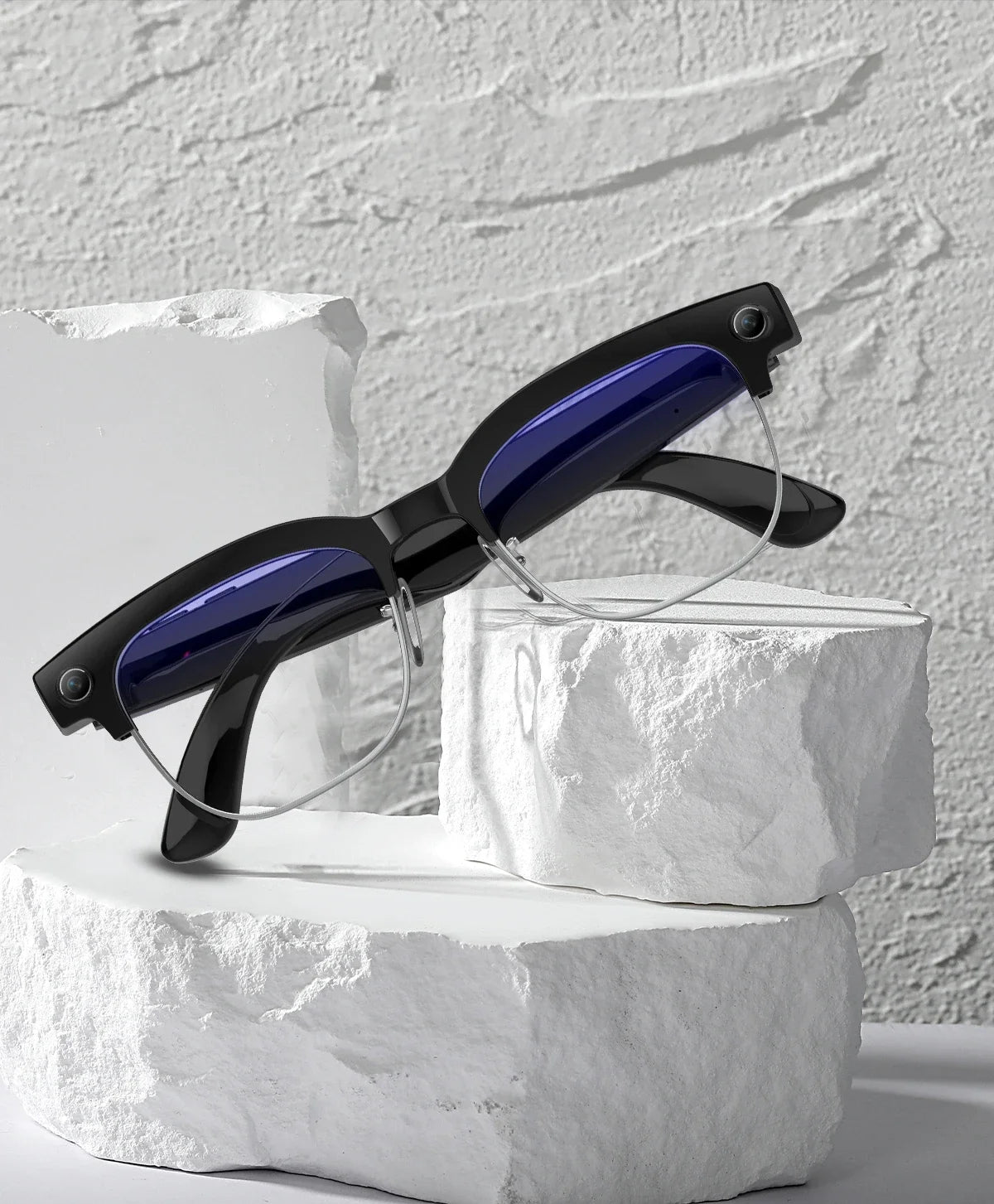 Sleek black smart glasses with integrated side cameras, blue-tinted lenses and silver rims, perched on white stones.