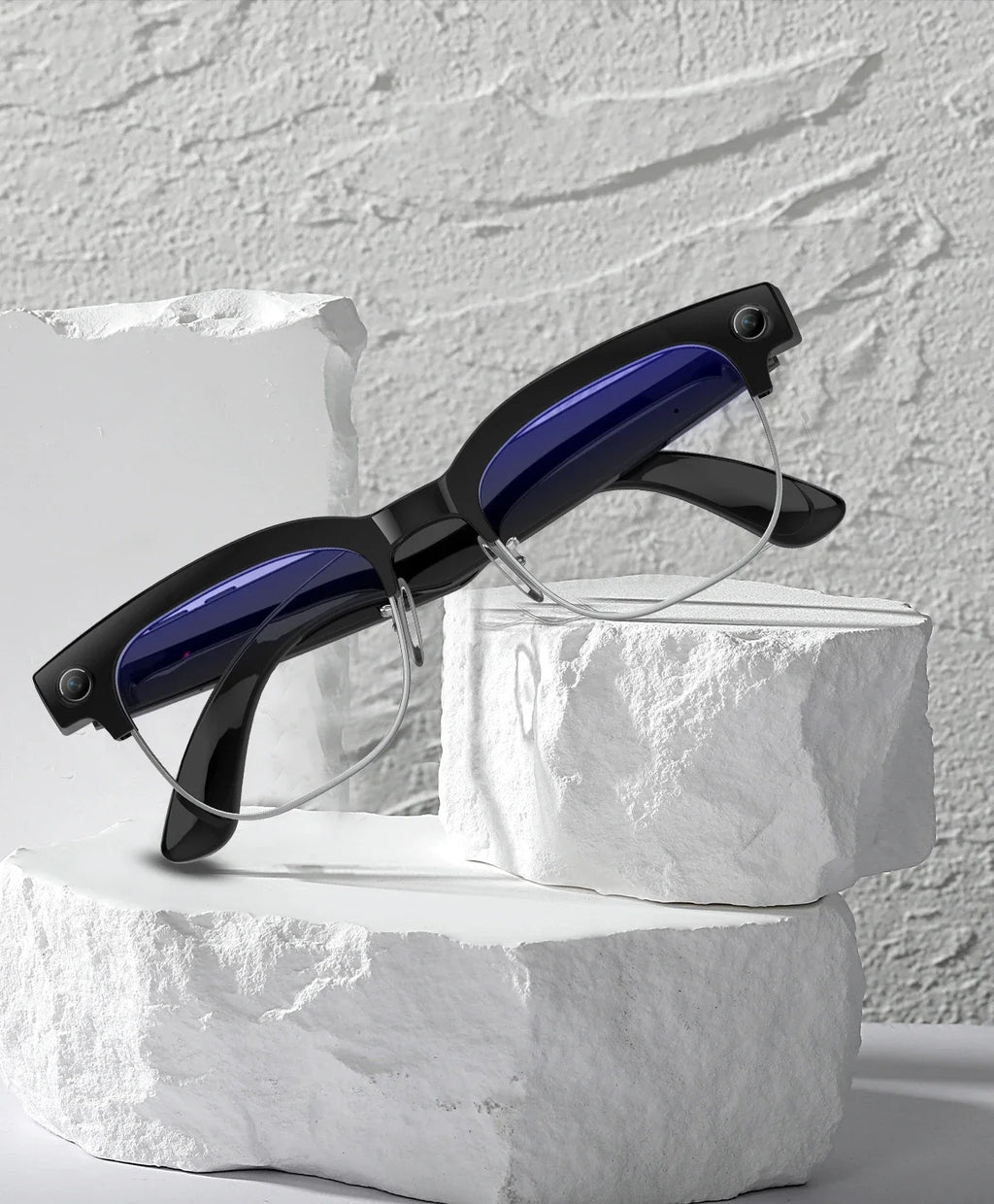 Black smart glasses with semi-rimless frames and built-in cameras, resting on white stone blocks.