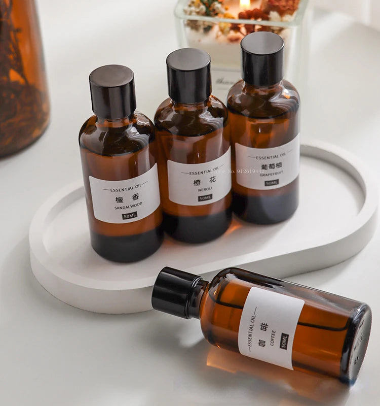 Four amber glass 50ml essential oil bottles with black caps and minimalist white labels on a white oval tray.