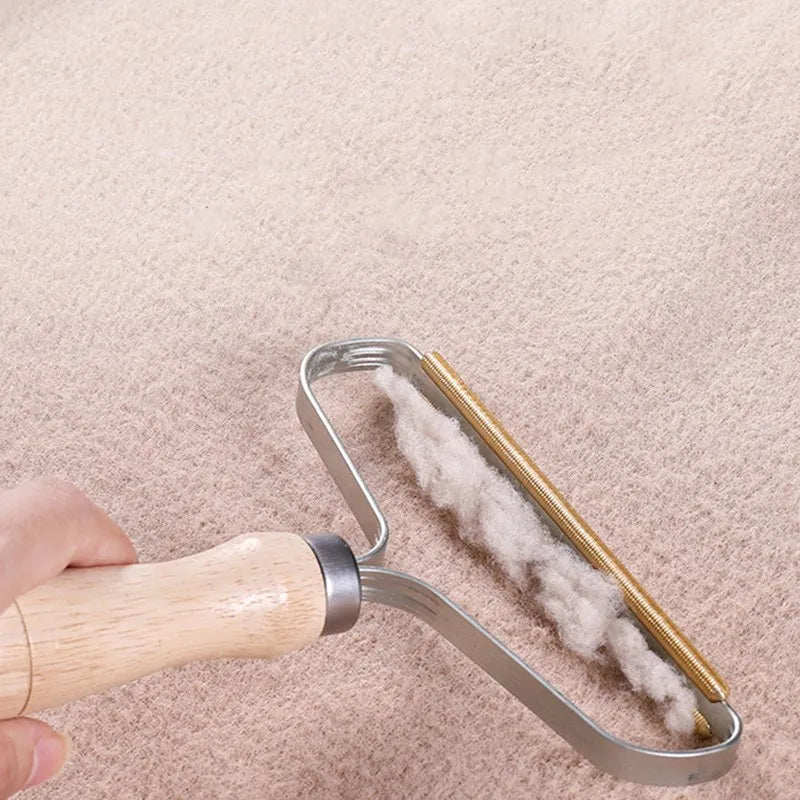 Handheld fabric shaver with a wooden handle and brass edge, removing white lint from a beige carpet.