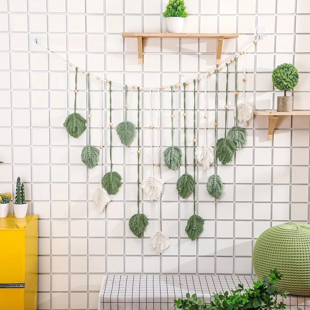 Boho macrame wall hanging featuring sage green and cream leaf motifs on a string with decorative wooden beads.