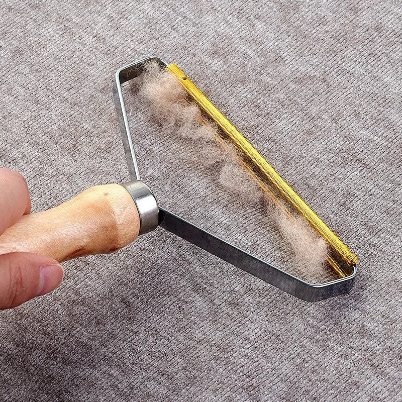 A hand using a portable lint remover with a wooden handle and gold metal head to remove fluff from a grey fabric.