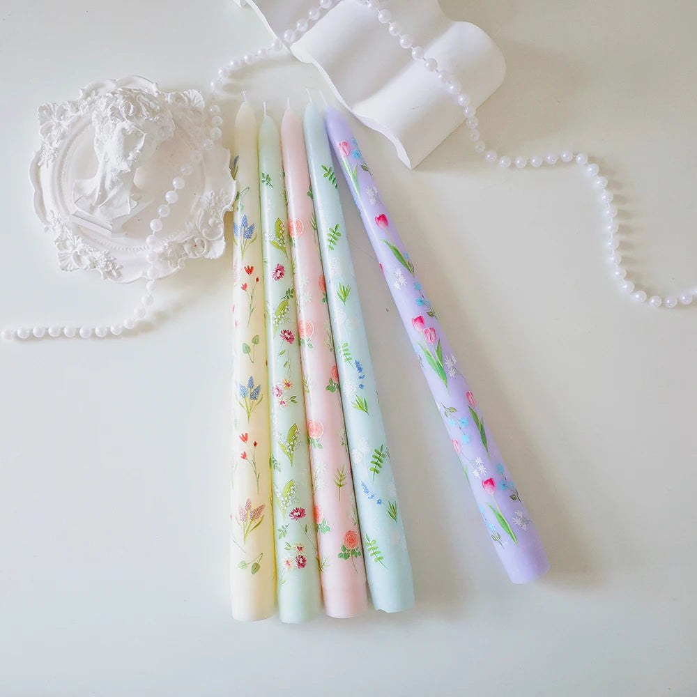 Set of five pastel taper candles in yellow, green, pink, blue, and purple, each featuring delicate floral prints.