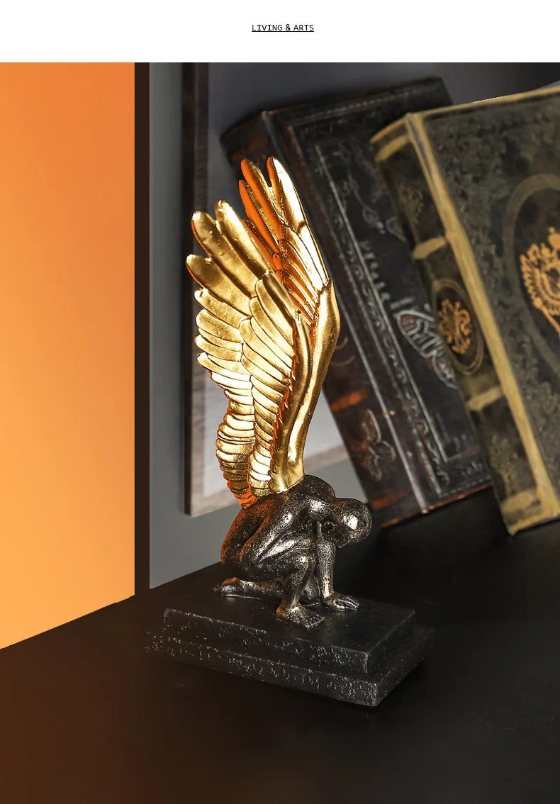 Decorative ornament of a kneeling figure with large, detailed gold wings on a textured black base.