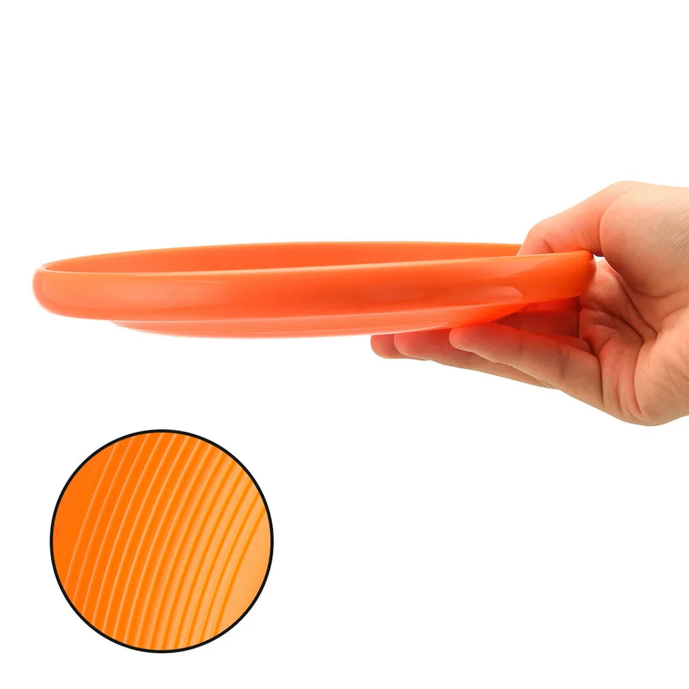 A hand holds a smooth, bright orange dog training disc with a textured, ridged underside for easy grip.
