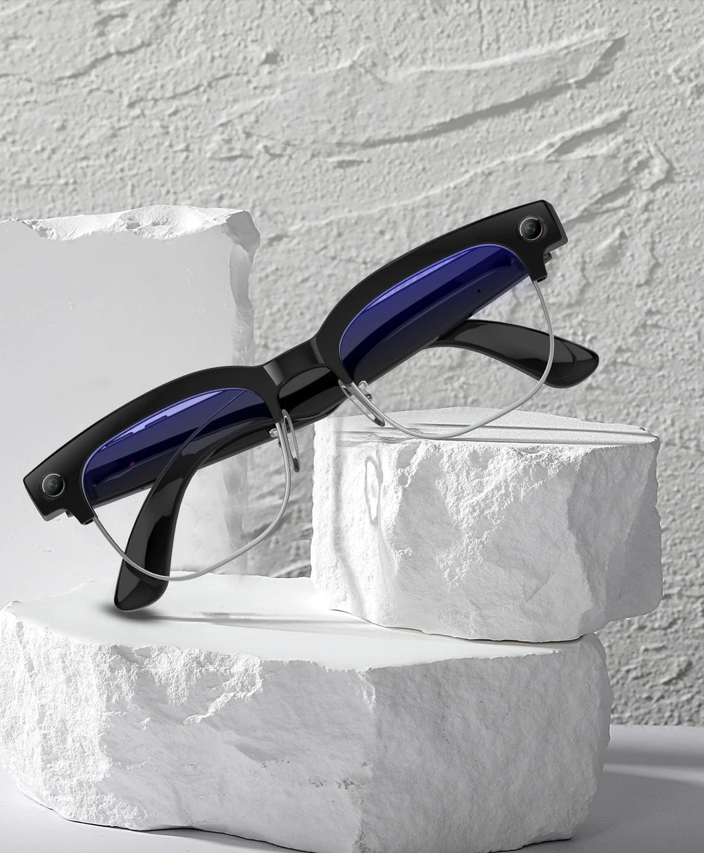 Black smart glasses with built-in cameras and blue-tinted lenses, resting on white stone blocks.